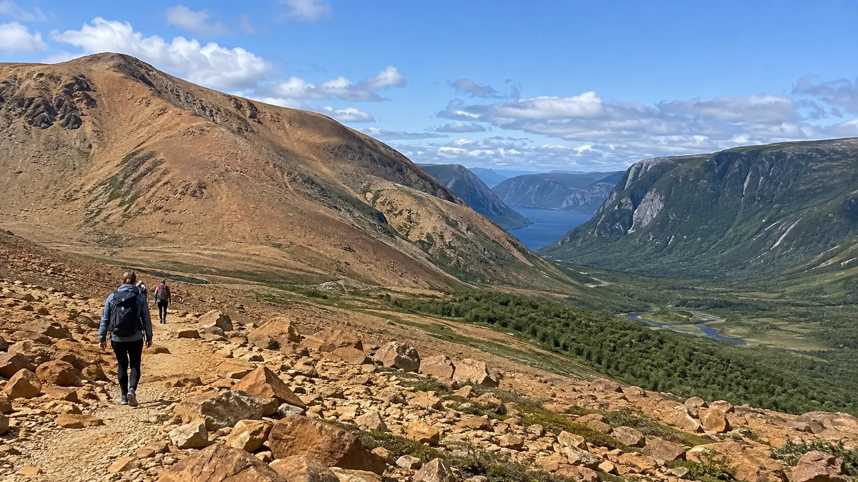 Hiker crossing the rust-colored Tablelands with Western Brook Pond cliffs beyond
