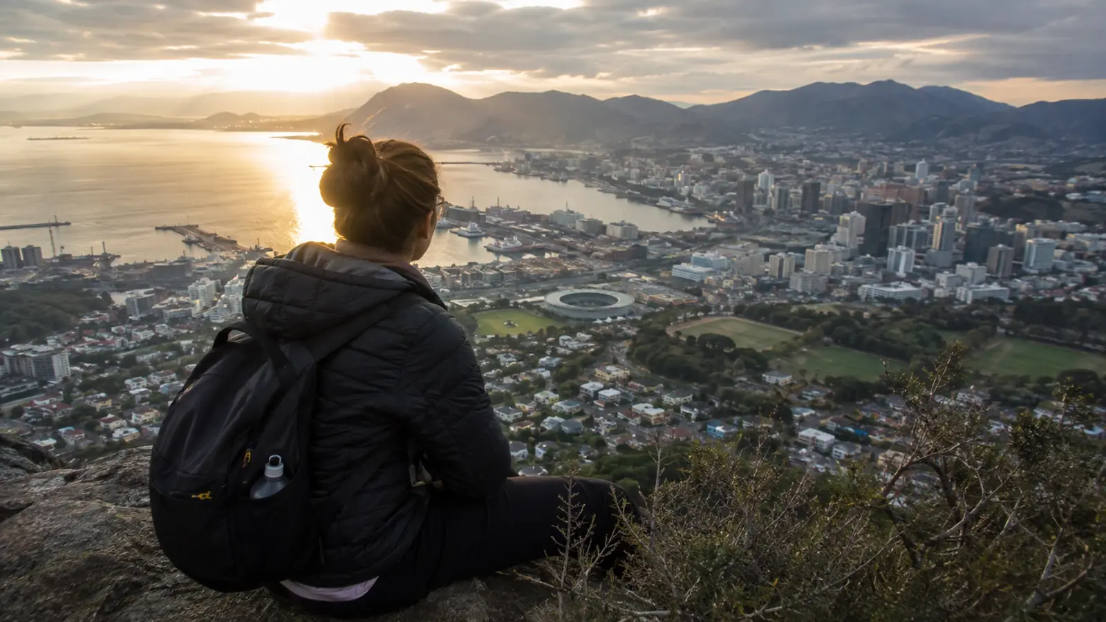 Woman with a backpack overlooking a coastal city at sunset