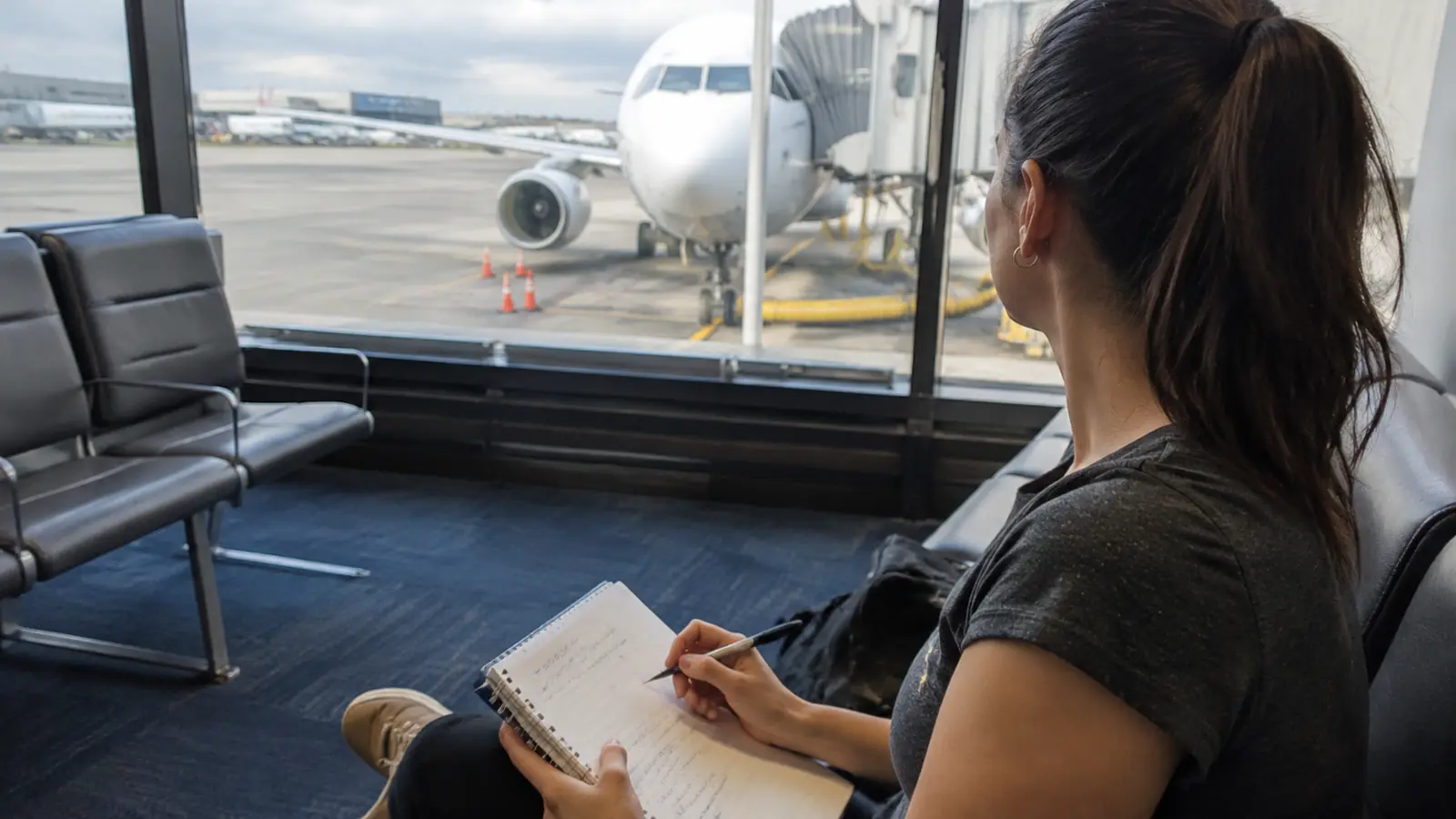 Woman writing in a notebook at an airport gate with an airplane outside