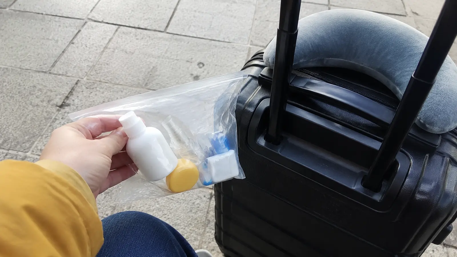 Hand holding a clear toiletry bag beside an open suitcase