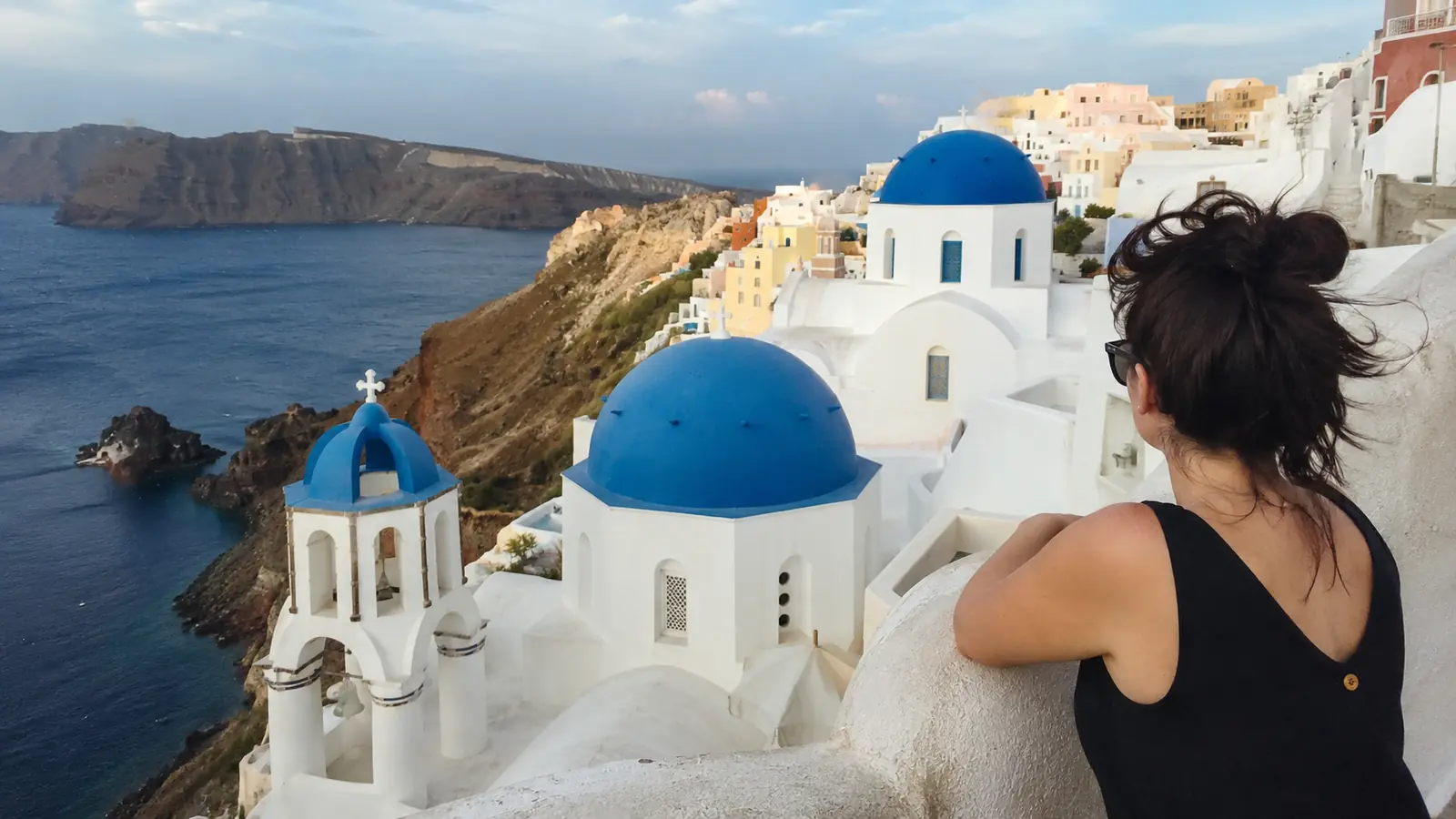Woman overlooking white cliffside buildings and blue-domed churches by the sea