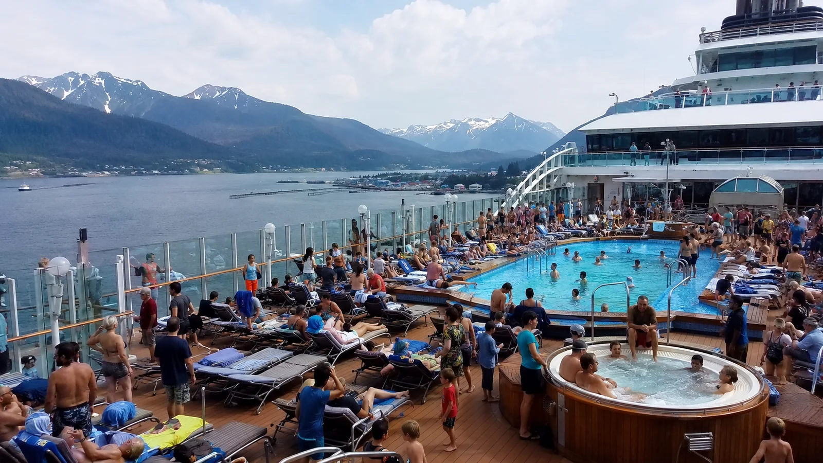 Crowded cruise ship pool deck with mountains in the background