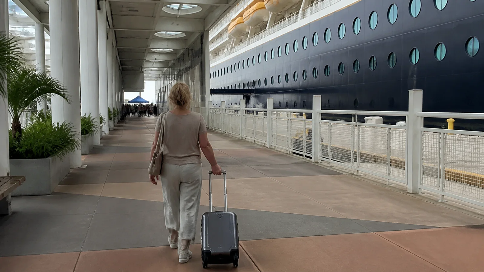 Traveler pulling a suitcase through a covered terminal beside a cruise ship.