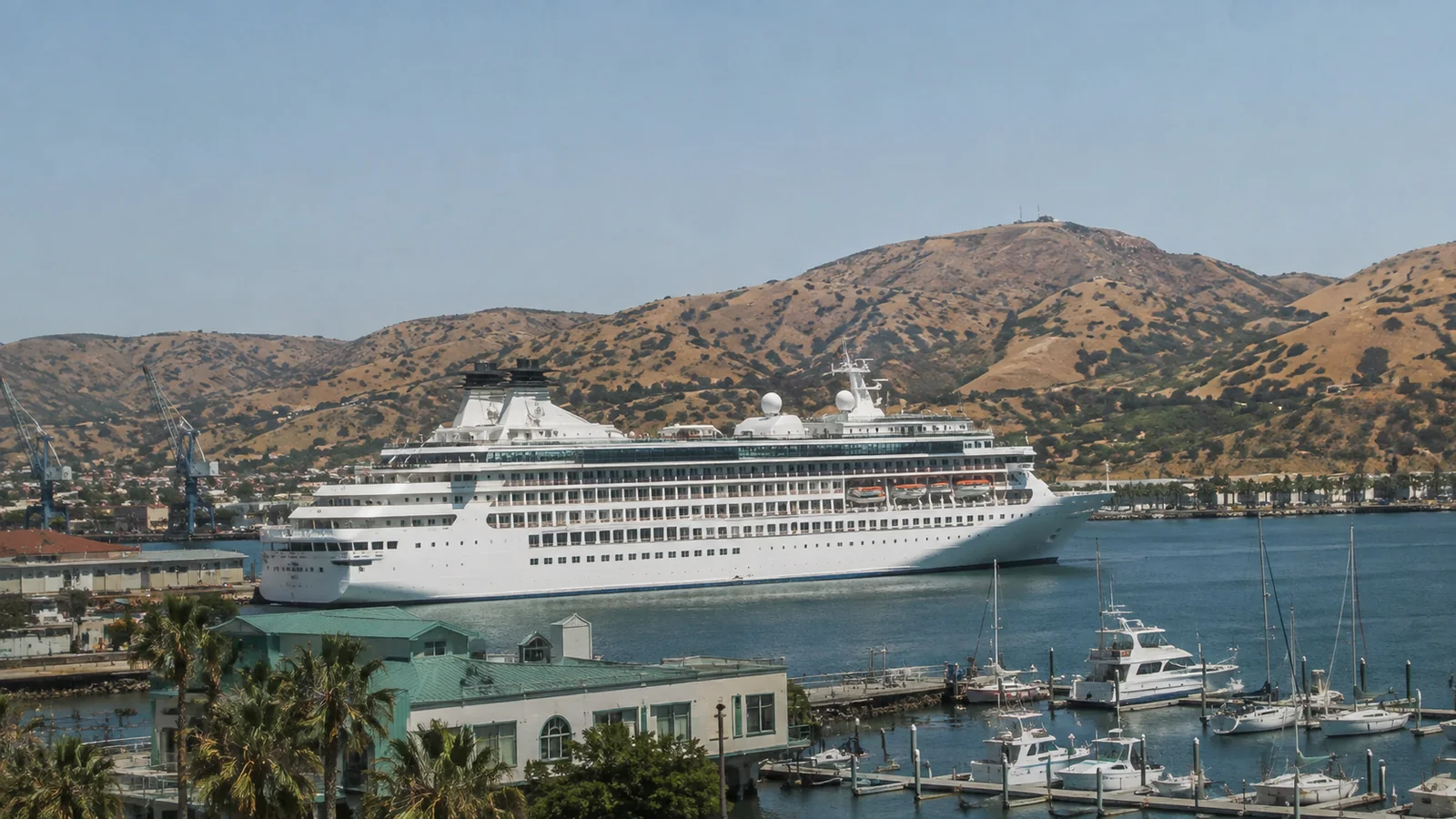 Cruise ship docked beside a marina with dry hills behind it.