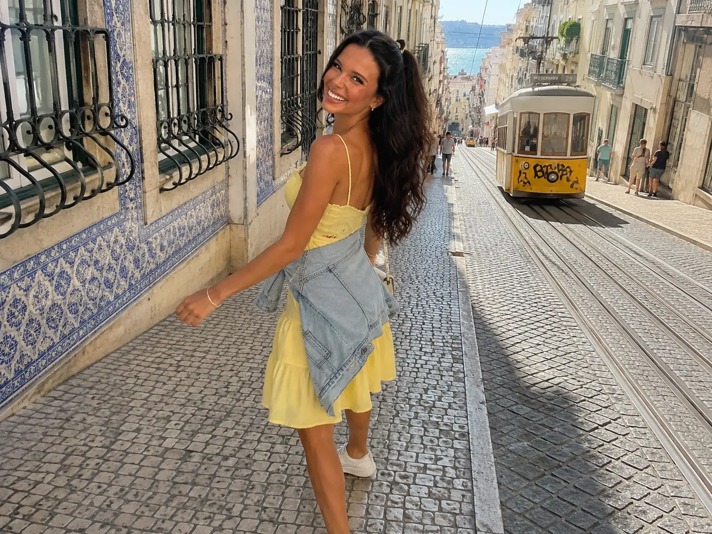 Ellie Simons walking beside a yellow tram in Lisbon