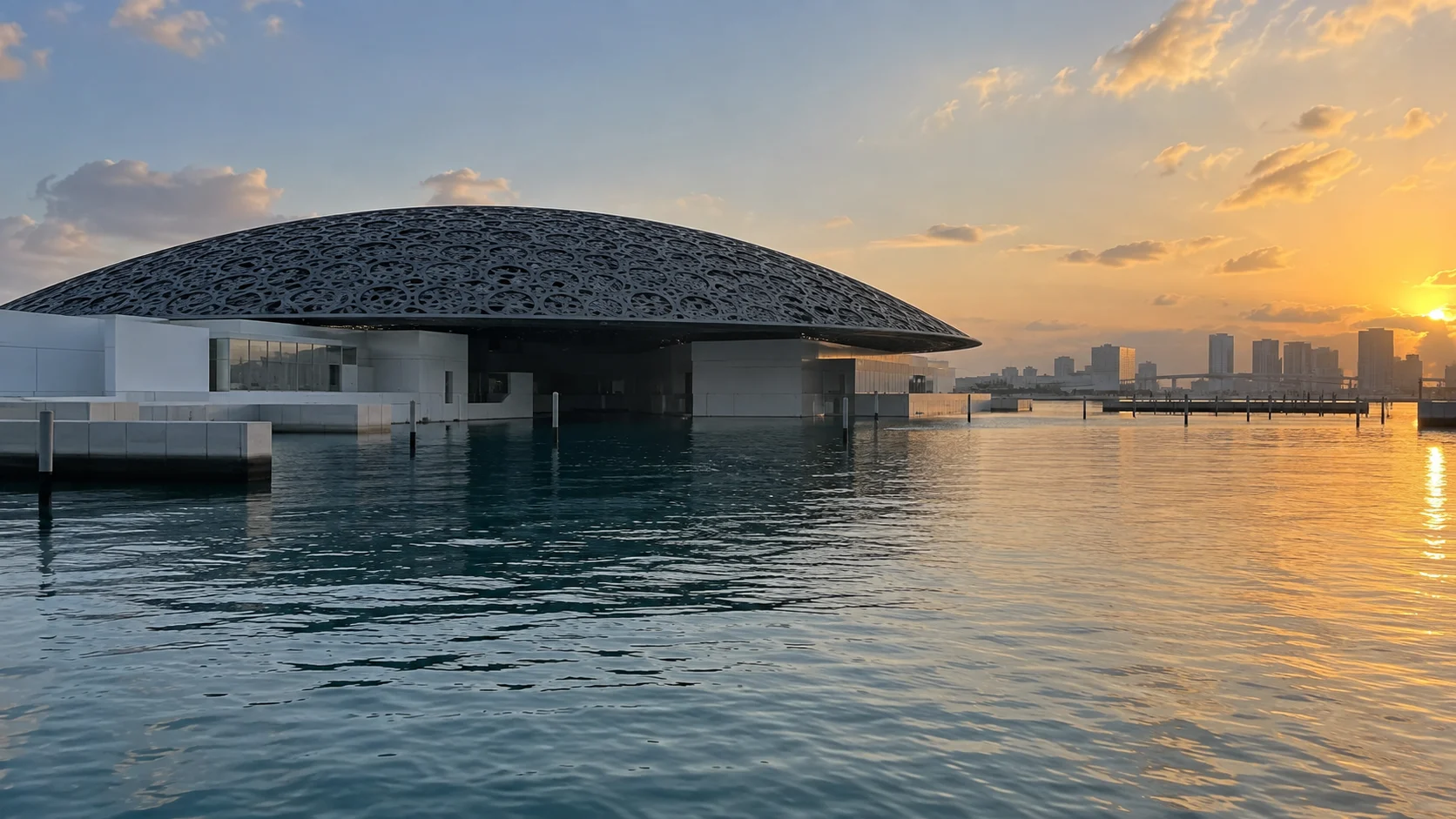 Louvre Abu Dhabi dome reflected in the waterfront at sunset