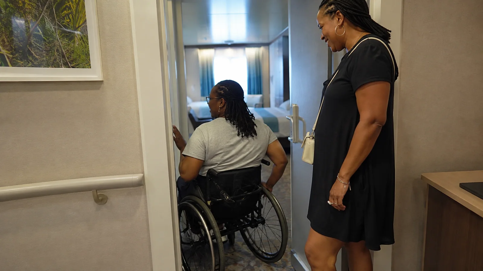 Wheelchair user enters a stateroom while a companion stands nearby.