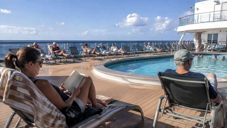 Passengers reading and relaxing beside an outdoor cruise ship pool