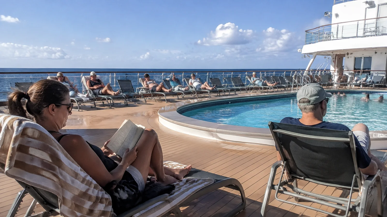 Passengers reading and relaxing beside an outdoor cruise ship pool