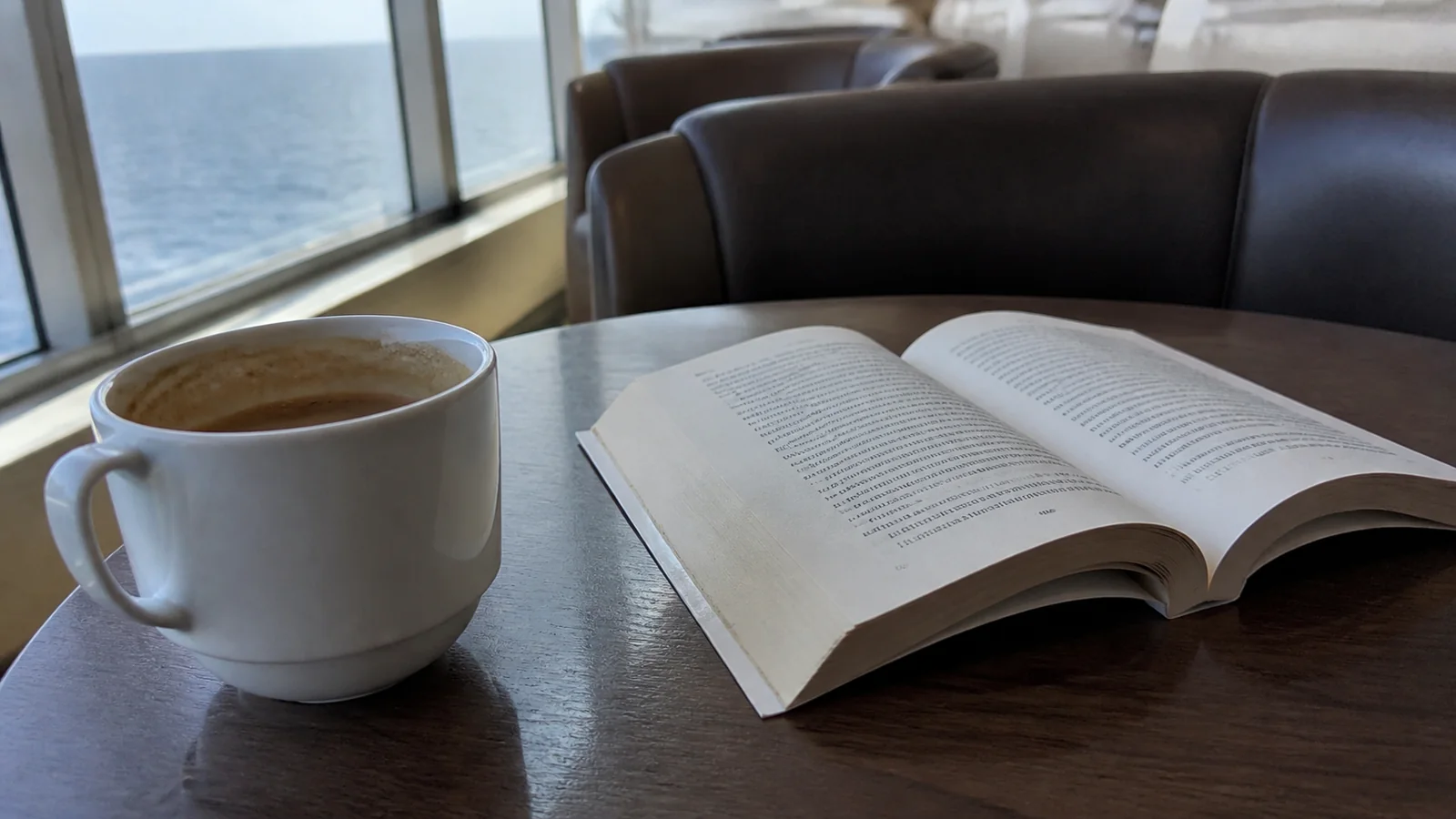 Coffee cup and open book on a table beside a ship's window