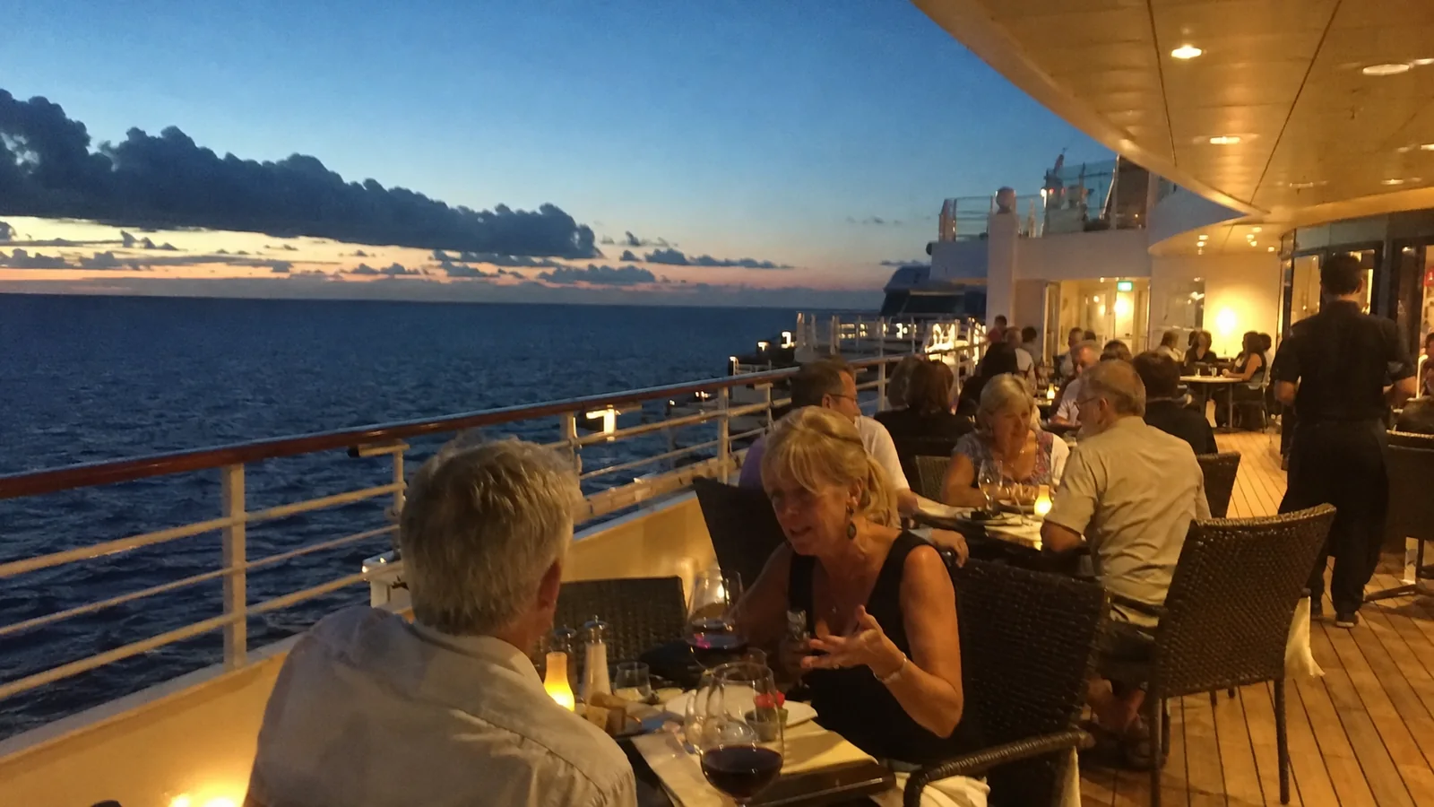 Passengers dining outdoors on a cruise ship at dusk