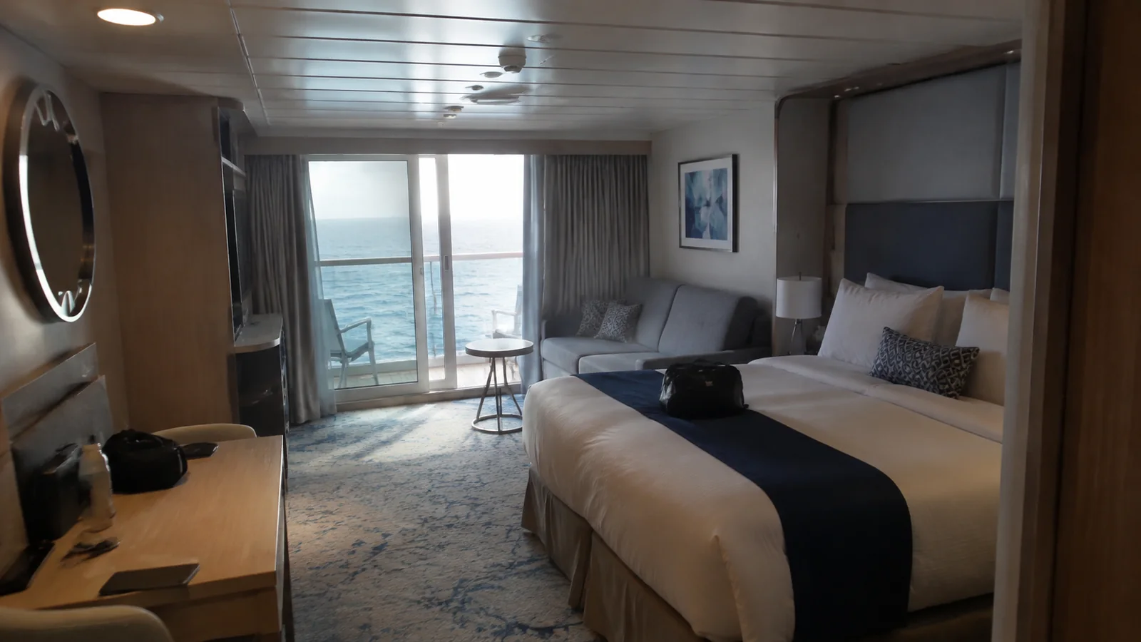Ship cabin with a bed, sofa, and balcony facing the sea.