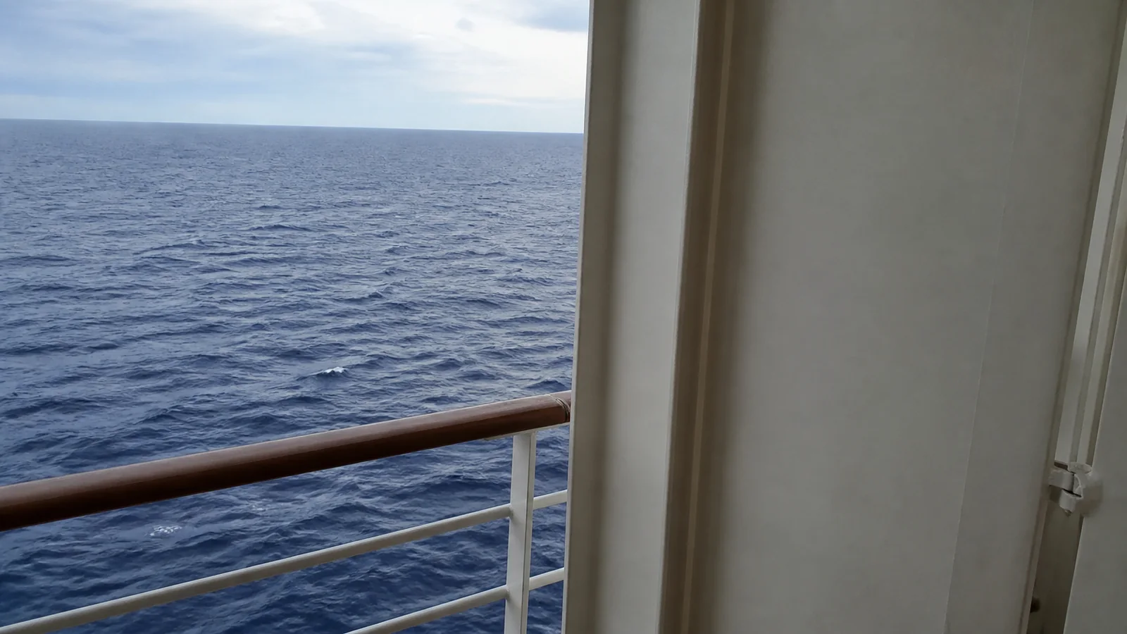 Ocean view partially blocked by a large structural panel beside a balcony railing.