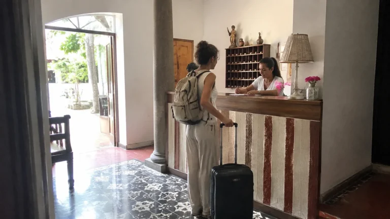 Traveler with a backpack and suitcase speaking to a hotel receptionist.