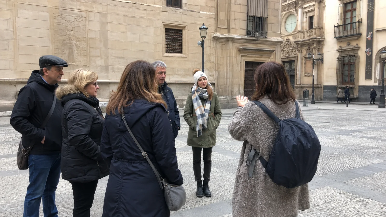 Small group listening to a guide in a historic stone-paved square.