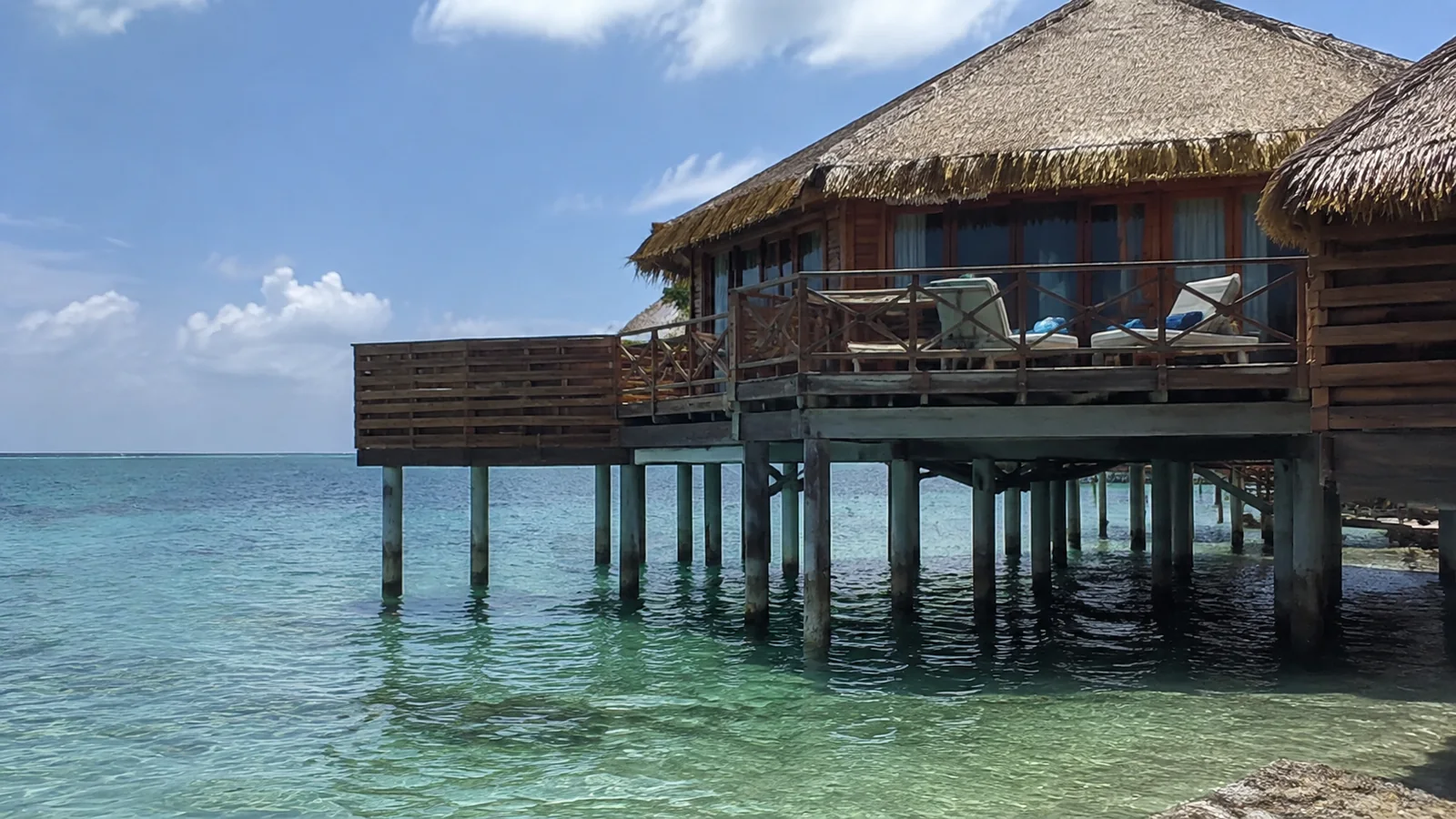 Thatched overwater bungalow with a private deck above clear turquoise water.