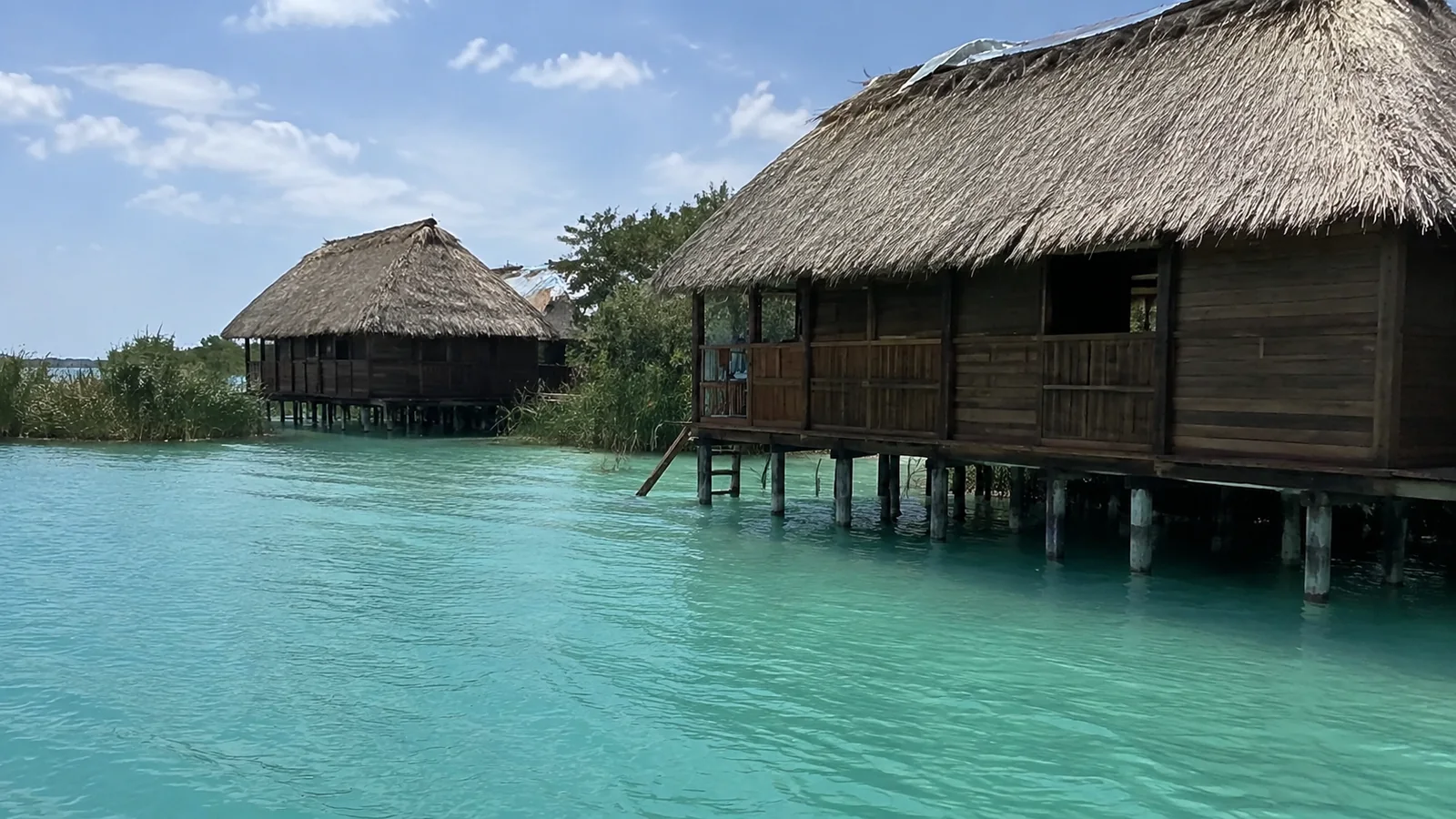 Thatched bungalows built on stilts beside a turquoise lagoon.