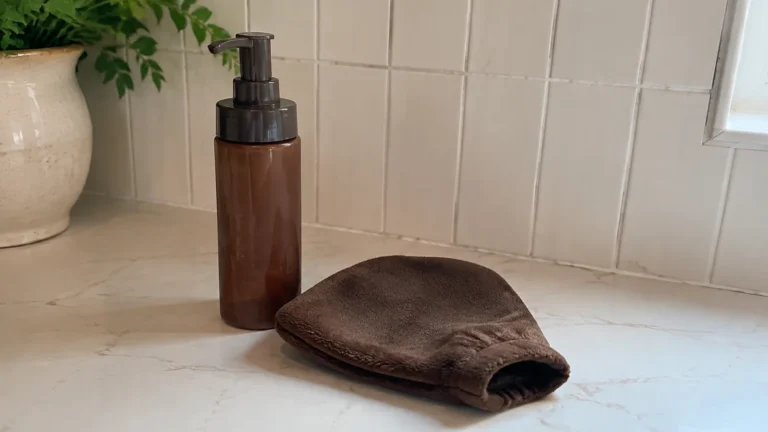 Amber pump bottle and brown applicator mitt on a bathroom counter.