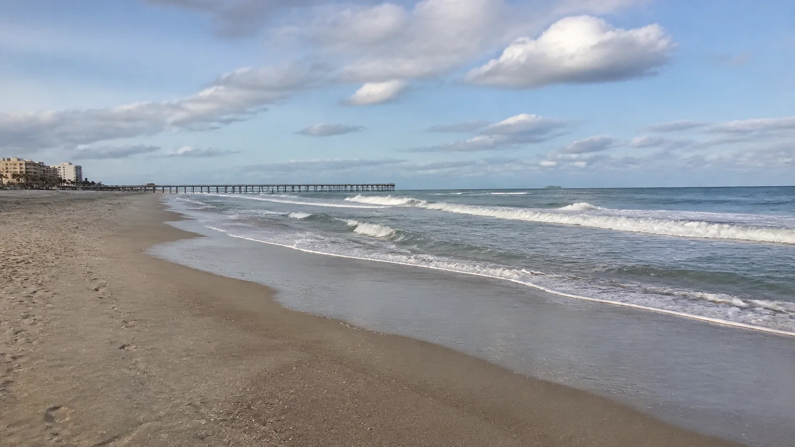 Waves breaking along a broad sandy beach with a distant pier.