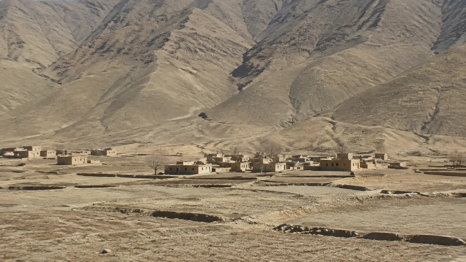 Low earth-colored buildings sit at the foot of barren mountains.
