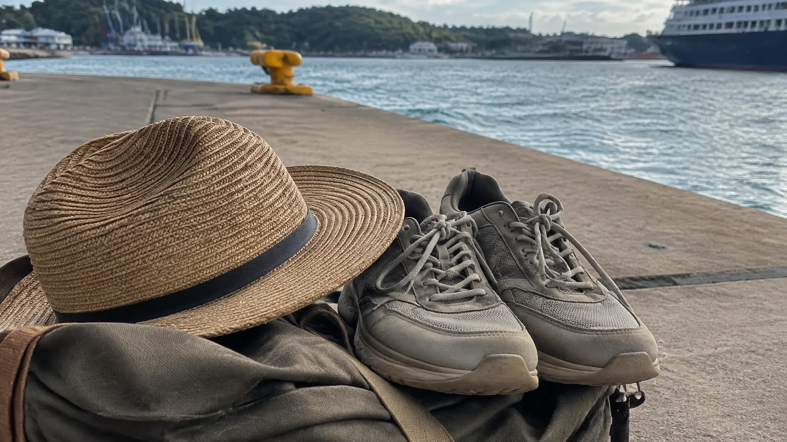 Sunhat and walking shoes resting on a bag beside a harbor