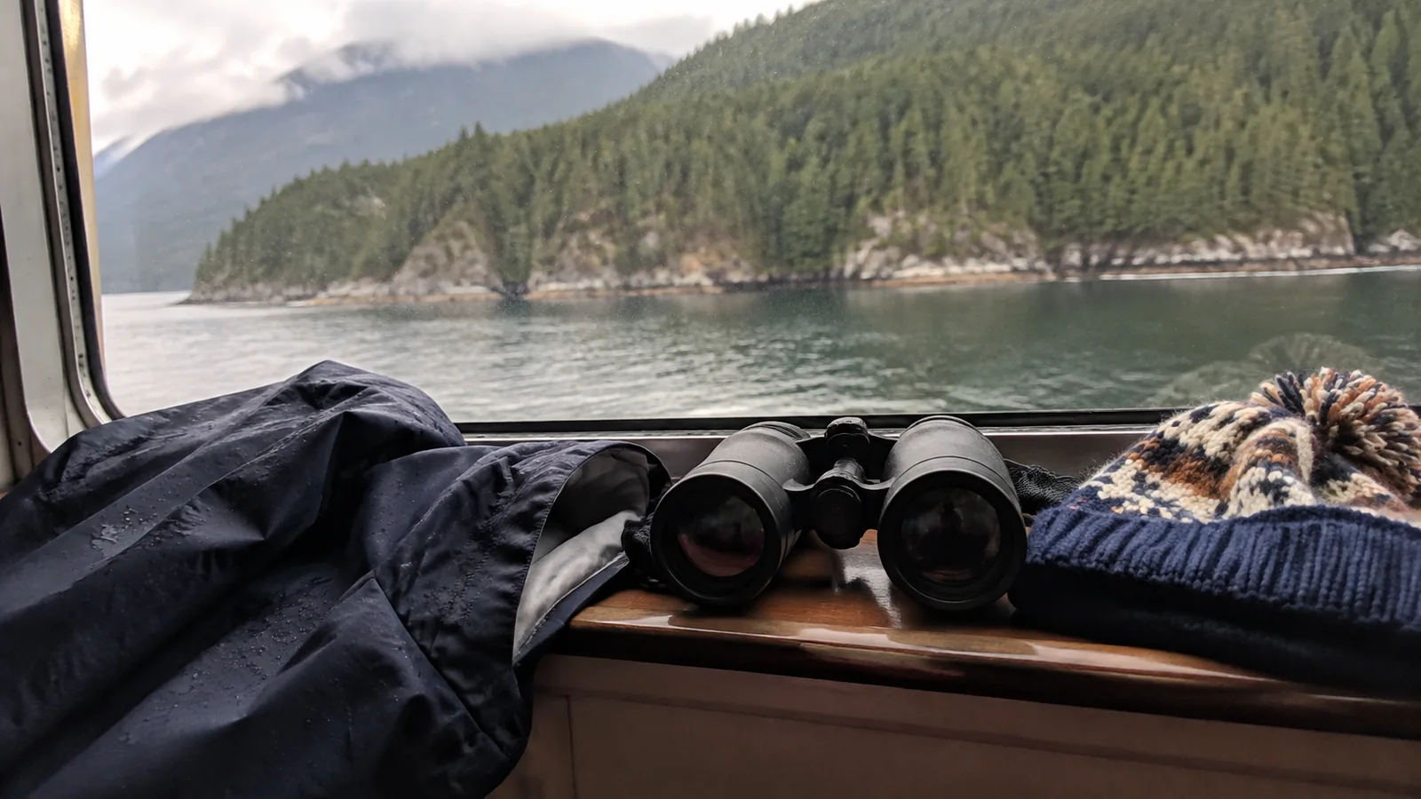 Binoculars, rain jacket, and knit hat beside a ship's window