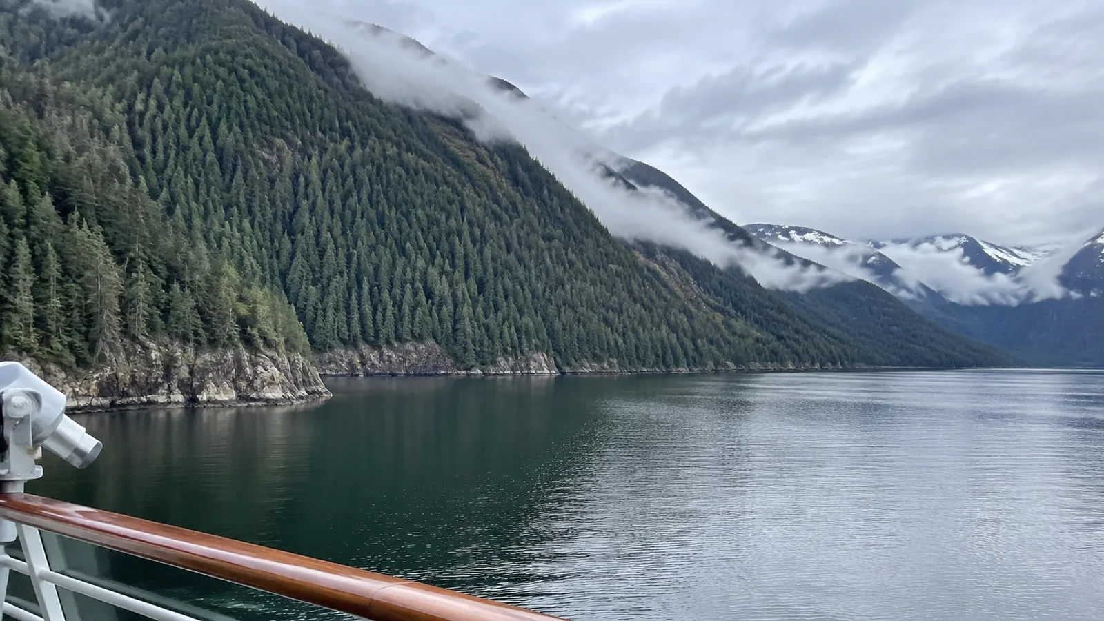 Misty forested mountains and calm fjord water viewed from a ship