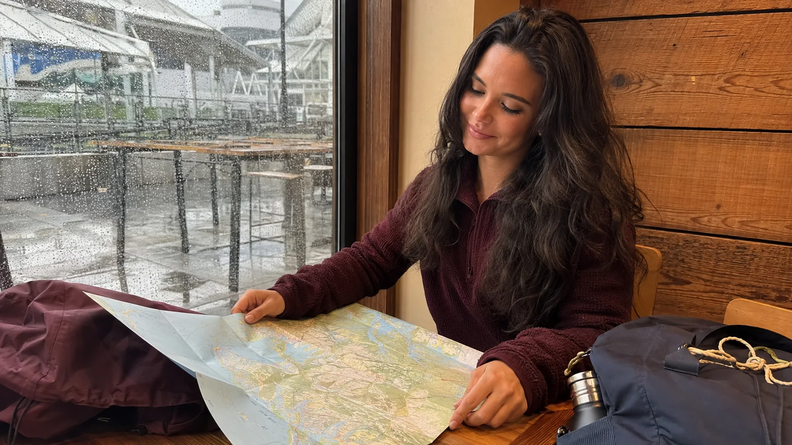 Woman studying a map at a table beside a rain-streaked window