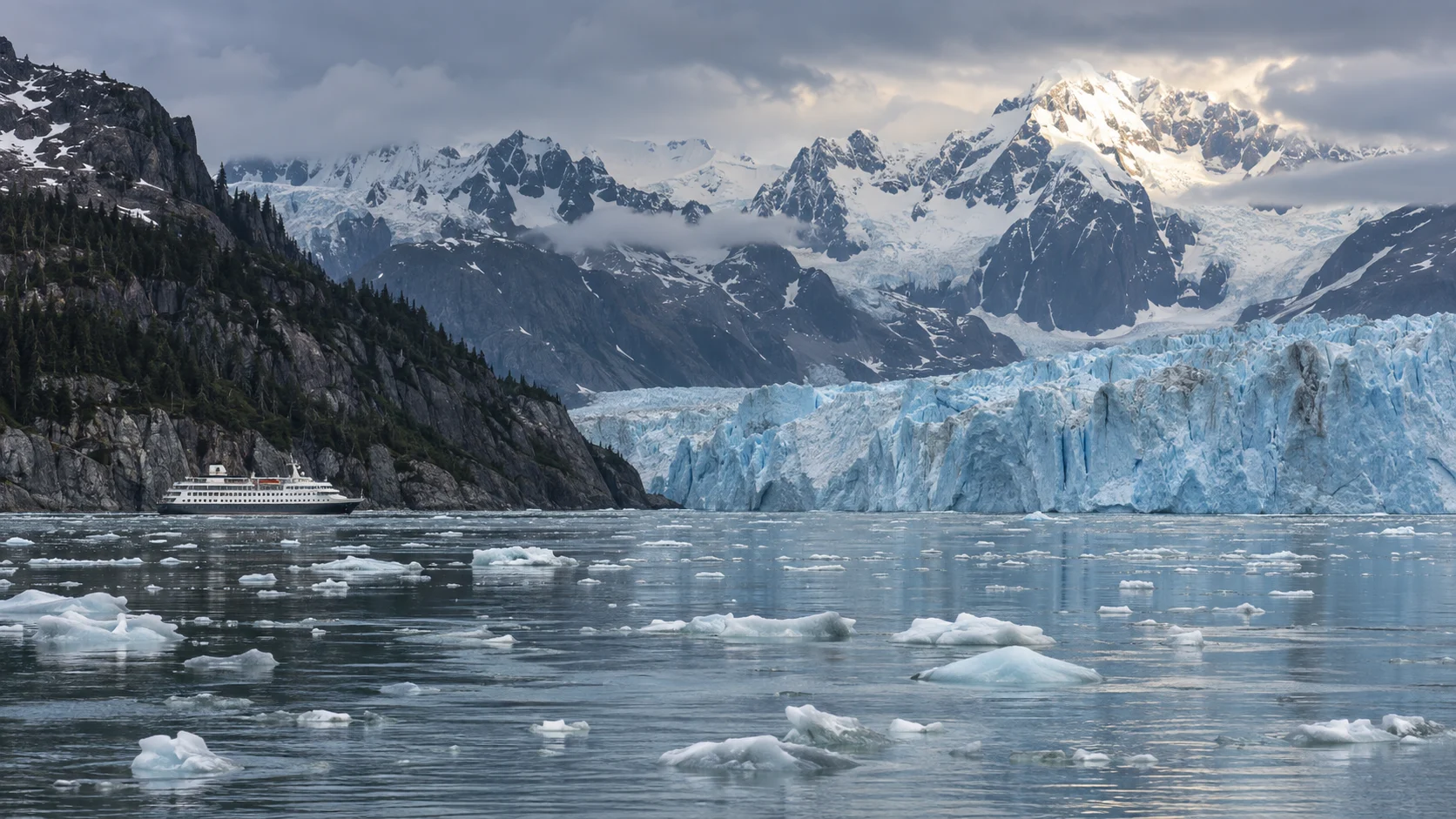 Small cruise ship sailing beside a blue tidewater glacier in Alaska's Glacier Bay