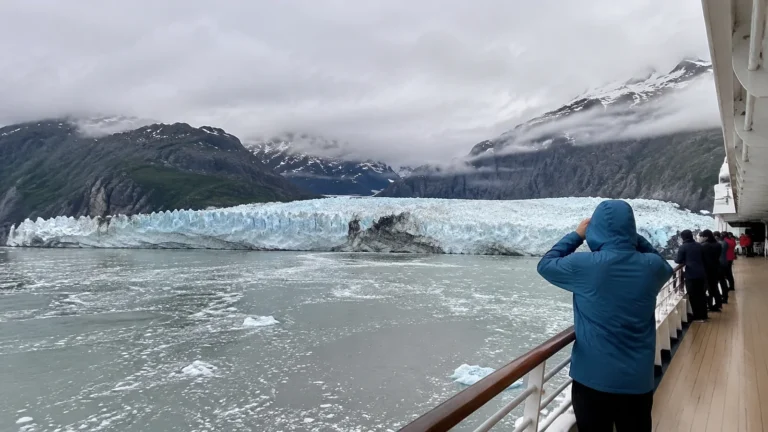 Hooded passenger photographing a glacier from a cruise ship deck