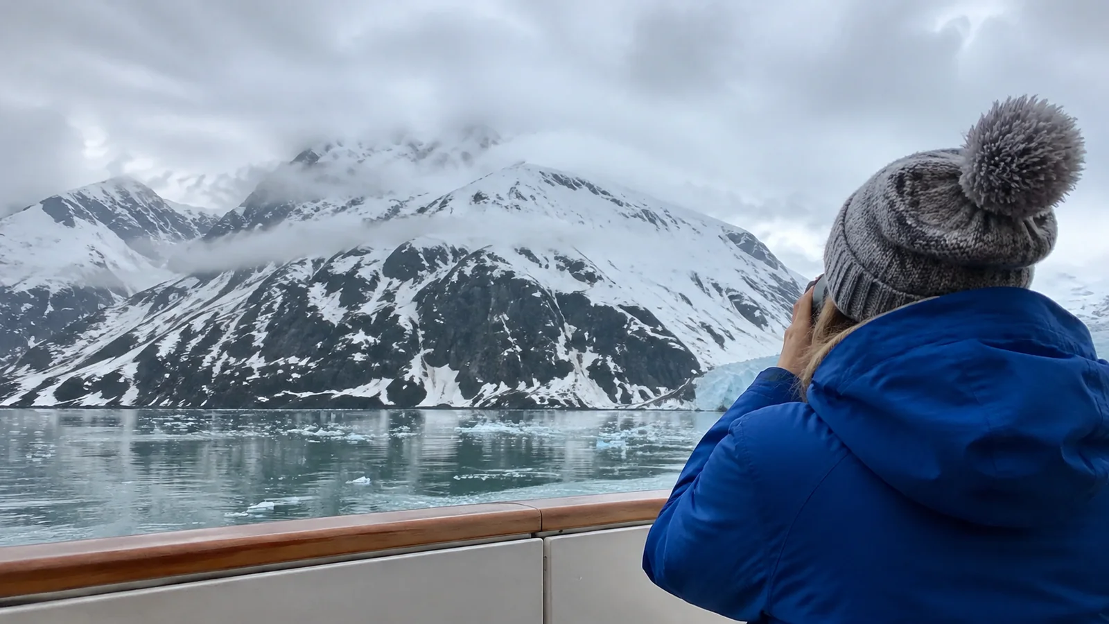 Hooded passenger looking toward snowy mountains and a glacier