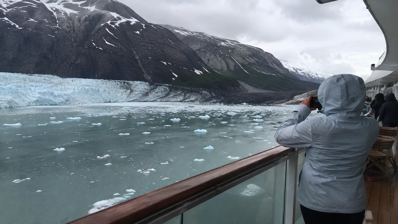 Hooded passenger photographing a glacier from a cruise ship