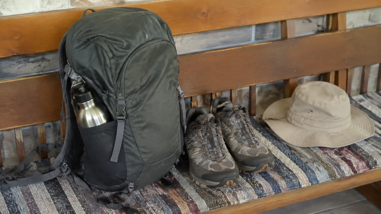 Backpack, hiking shoes, water bottle, and sun hat rest on a bench.
