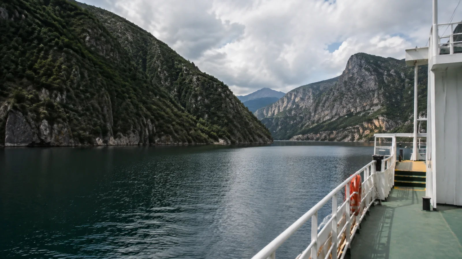 View from a boat across a narrow lake between steep wooded mountains.