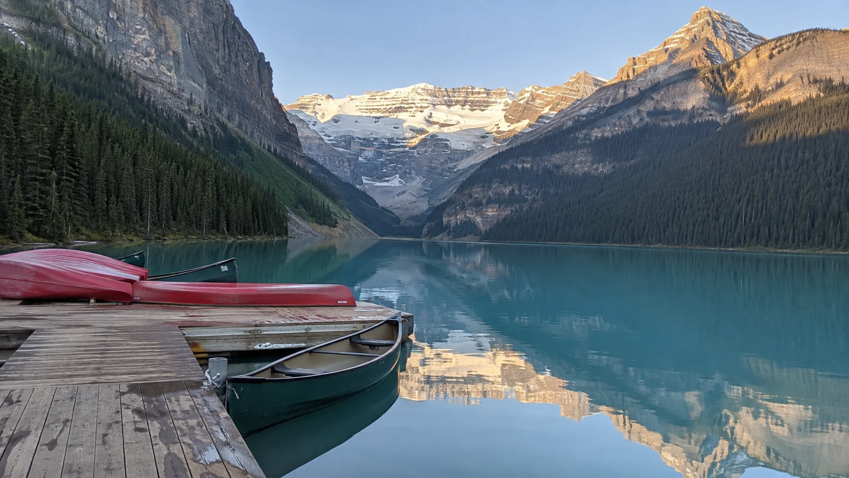Canoes at a quiet dock on turquoise Lake Louise beneath Victoria Glacier