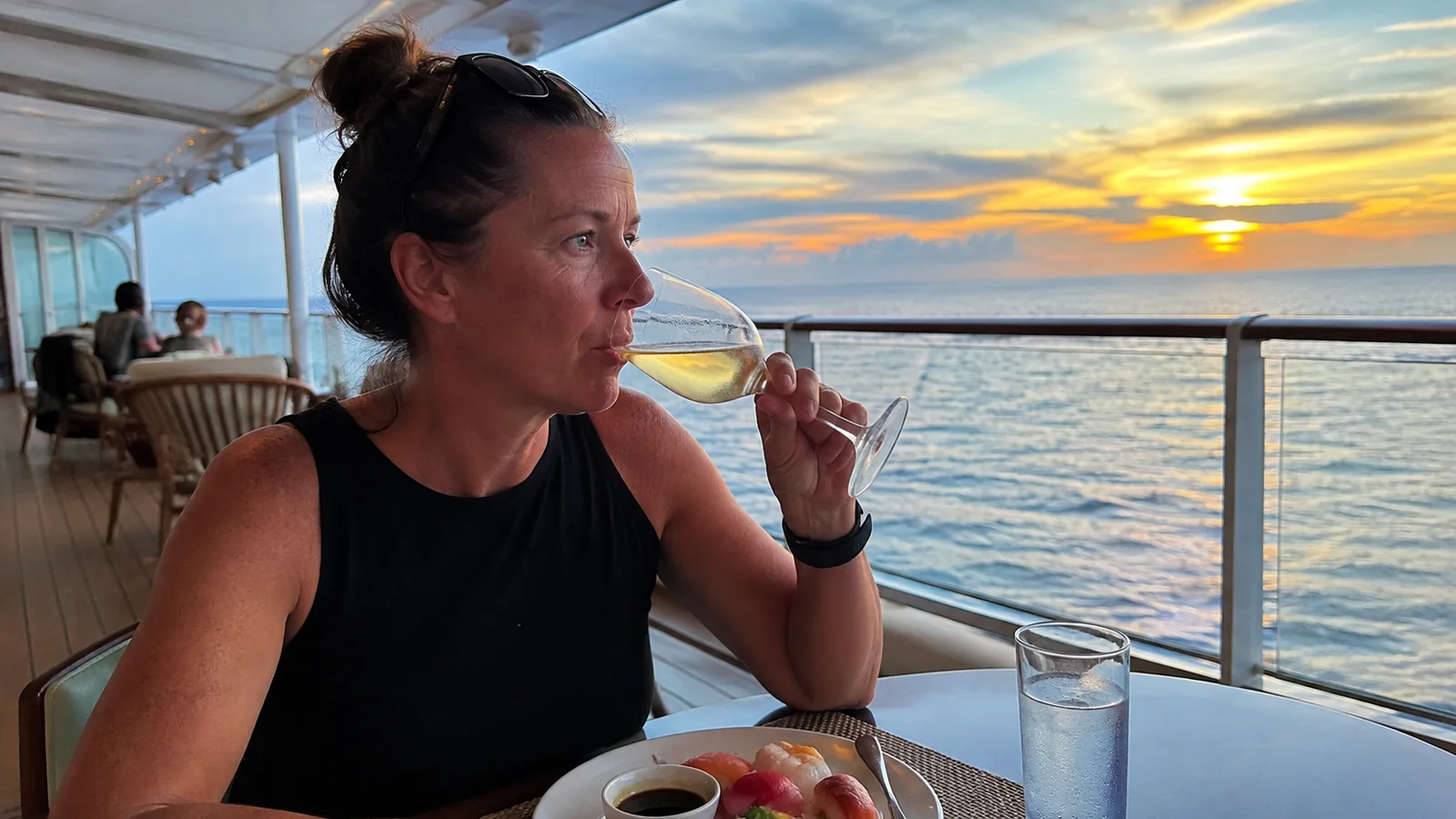 Woman dining outdoors on a cruise ship and holding a wine glass at sunset