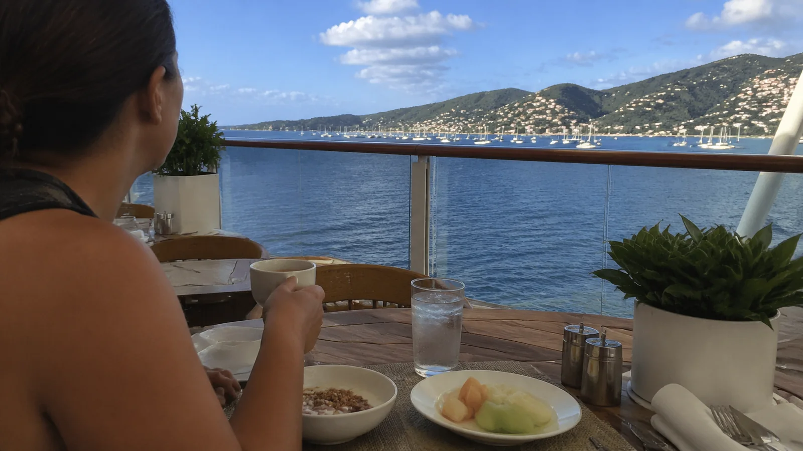 Person eating breakfast on a balcony overlooking a coastal town
