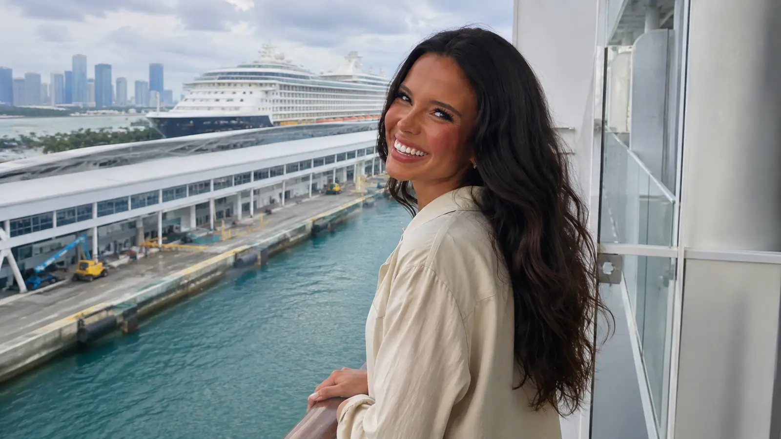 Smiling woman walking through a cruise terminal with docked ships behind her