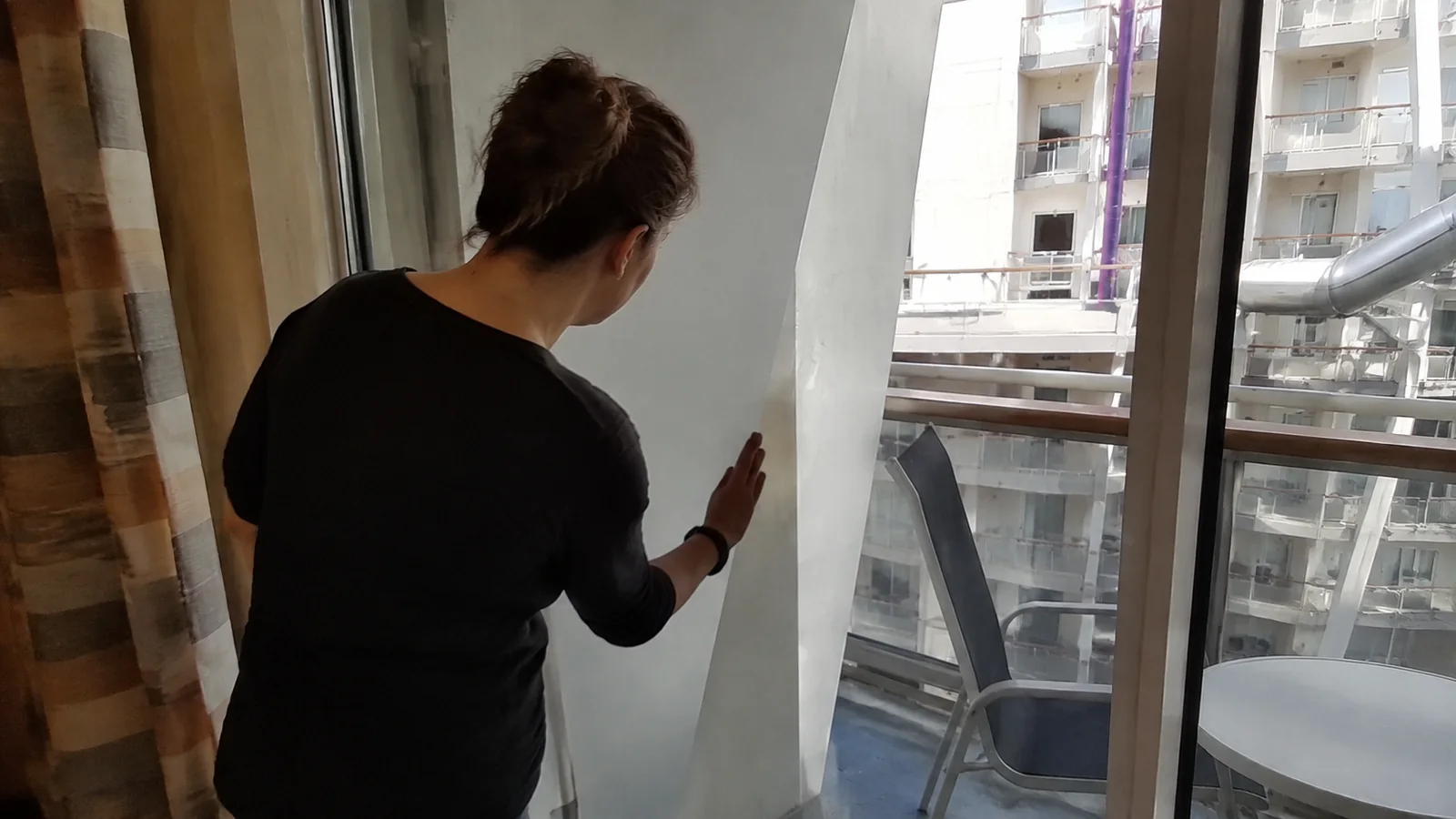 Woman looking past a balcony partition toward cabins across a ship's interior courtyard