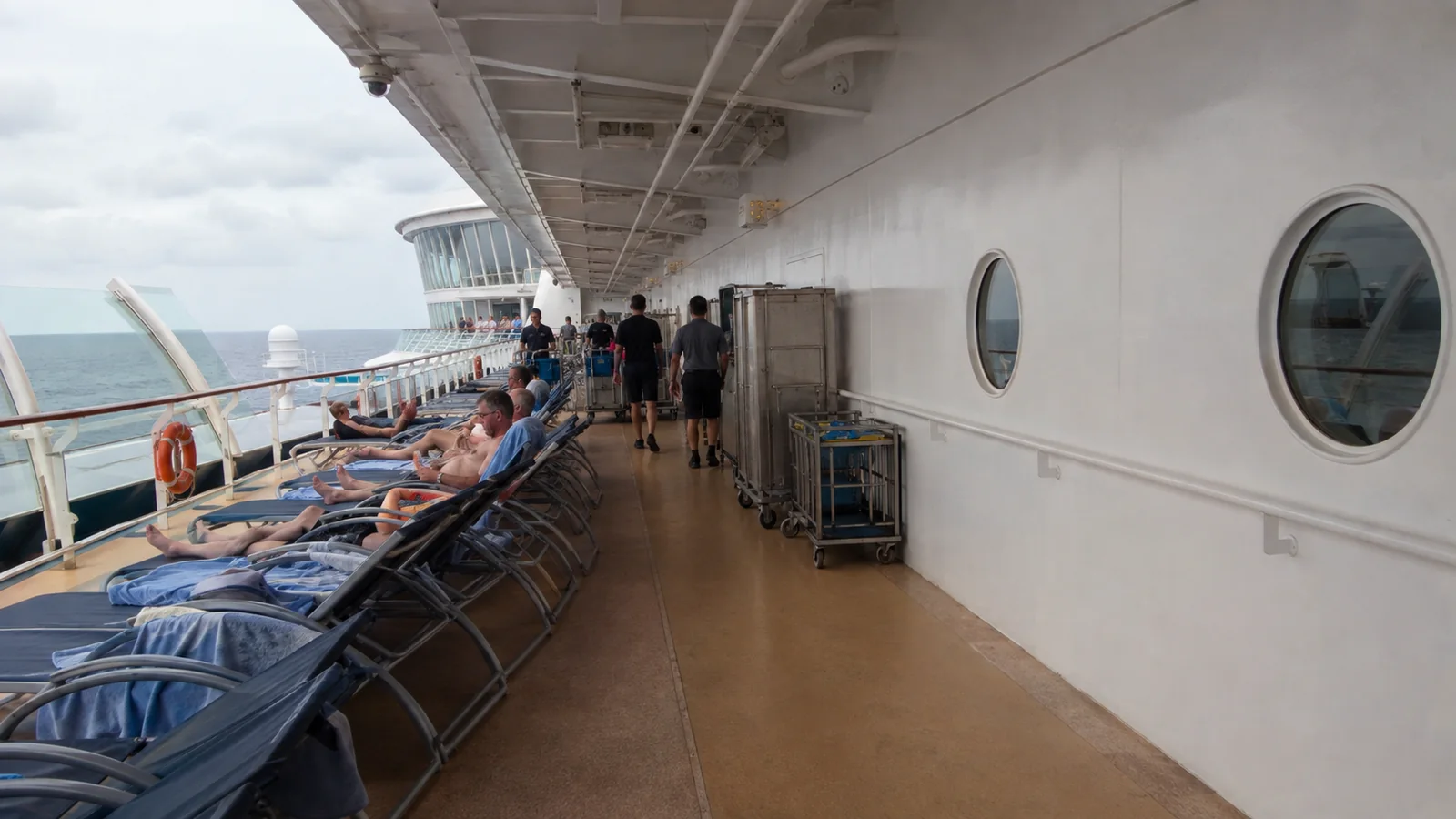 Passengers relaxing on lounge chairs along a covered cruise ship promenade