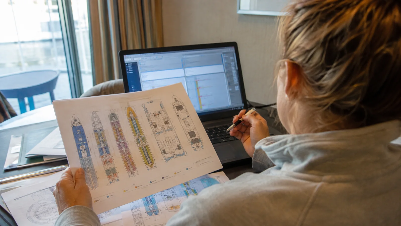 Woman reviewing a printed cruise ship deck plan beside a laptop