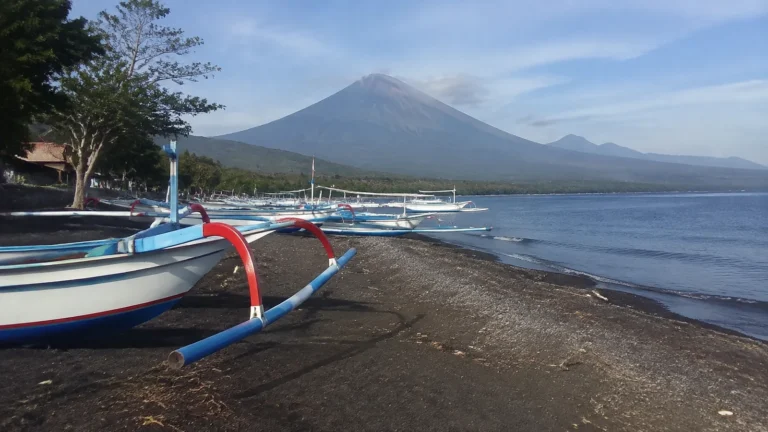Outrigger fishing boats on a dark beach below a volcano.