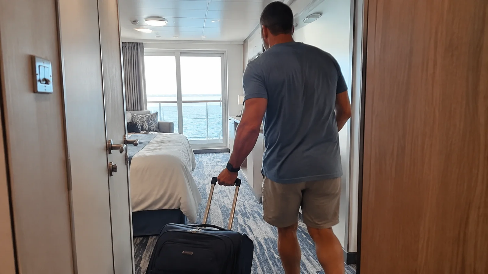 Man wheeling a suitcase into a balcony cabin.
