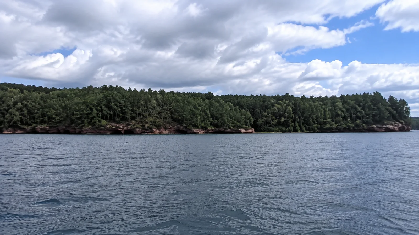 Forested island with low rocky cliffs across open water.