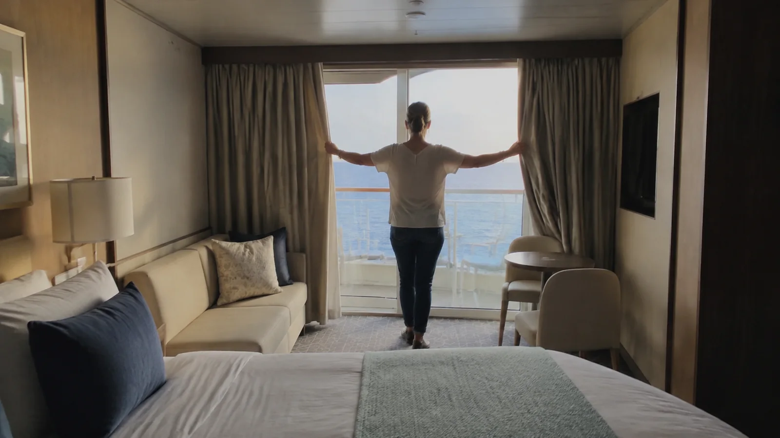 Passenger opens curtains to reveal a balcony and ocean view.