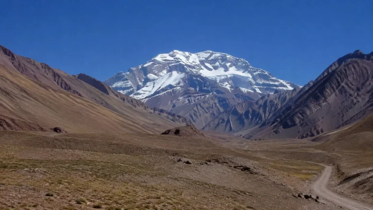 Snow-covered mountain rises above a broad barren valley.
