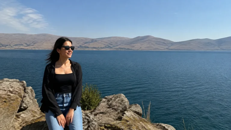 Woman stands on a rocky overlook above a blue mountain lake.