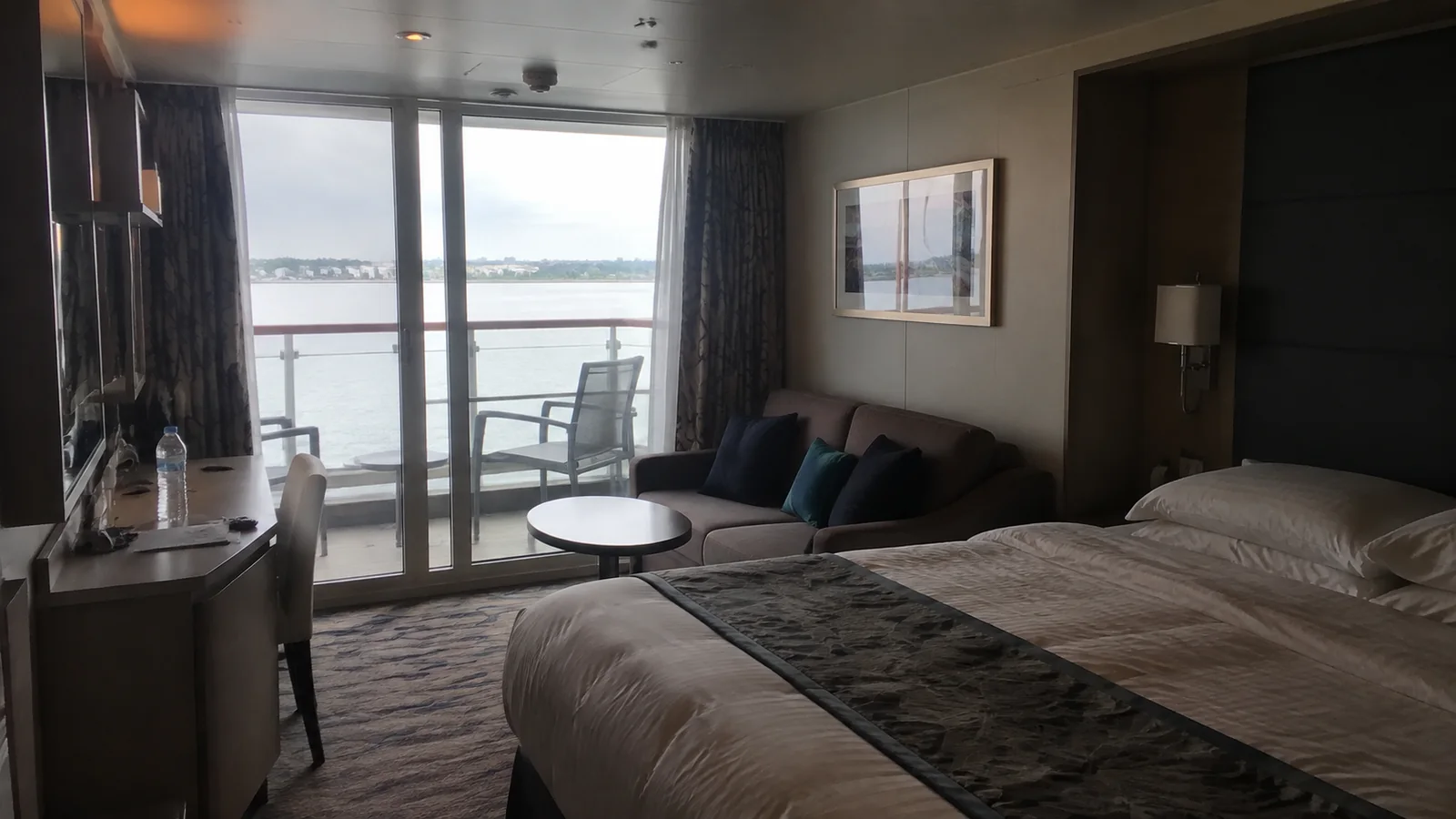 Cruise cabin with a double bed, sofa and glass doors opening onto a balcony.