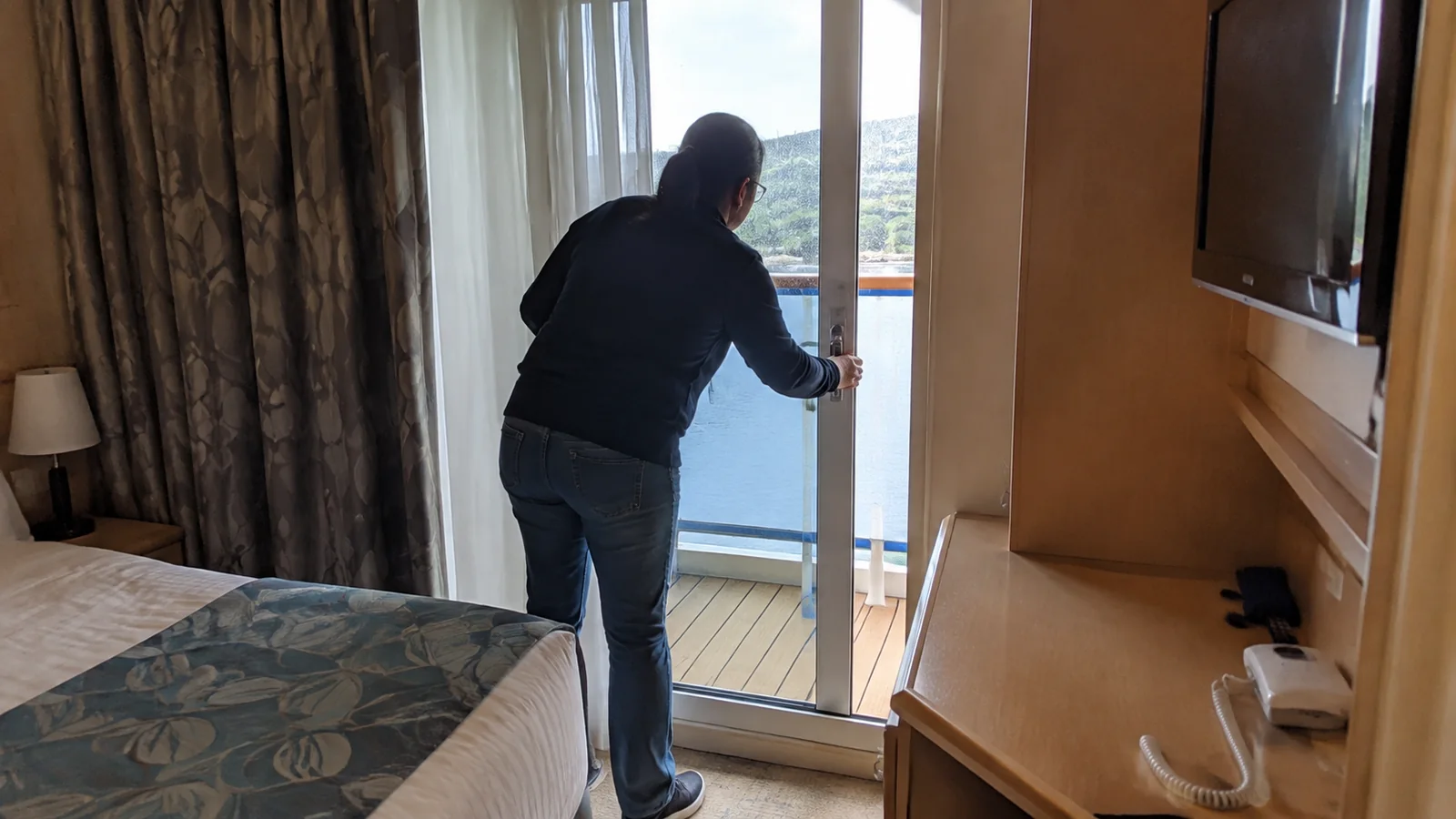 Passenger opening the balcony door in a cruise cabin.