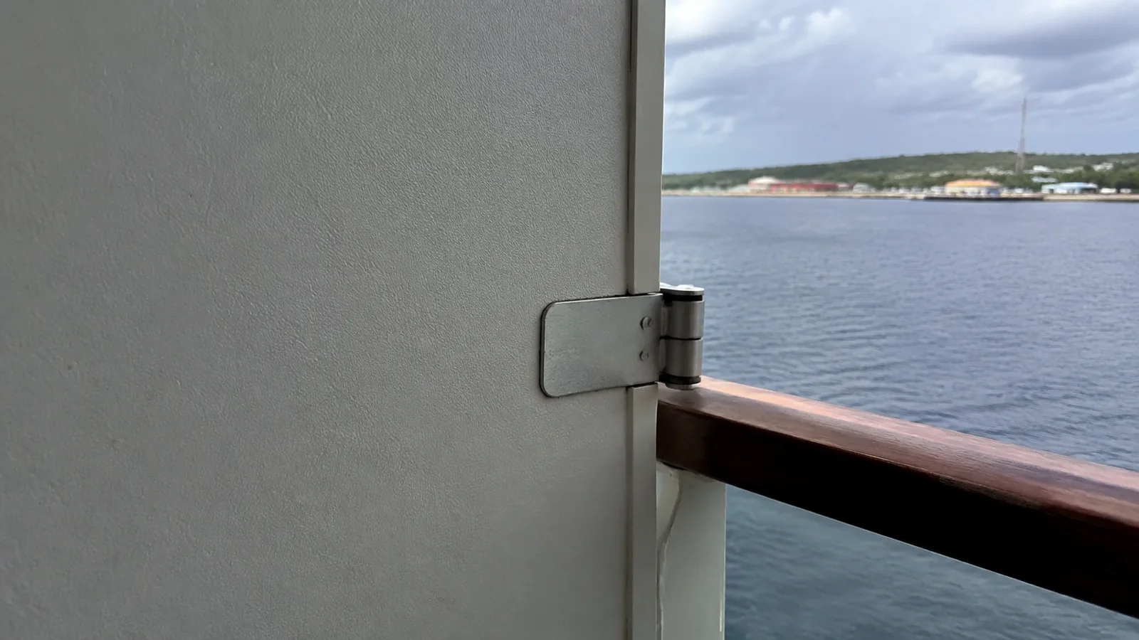 Balcony partition hinge beside a wooden railing overlooking the water.